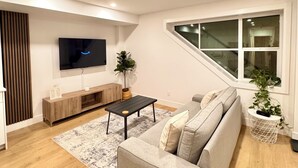 A modern living room with a sofa, TV, wooden floor, and a window.