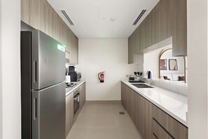 A modern kitchen with stainless steel appliances, wooden cabinets, and a white countertop. - Silkhaus Vacation Homes Prime 2BR in Yas Golf Collection (Abu Dhabi)