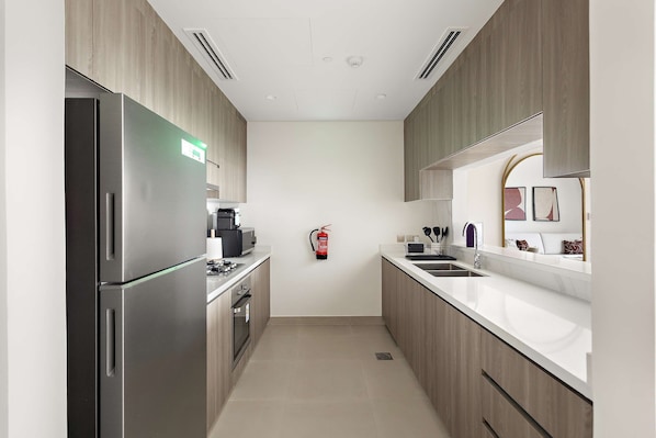 A modern kitchen with stainless steel appliances, wooden cabinets, and a white countertop. - Silkhaus Vacation Homes Prime 2BR in Yas Golf Collection (Abu Dhabi)