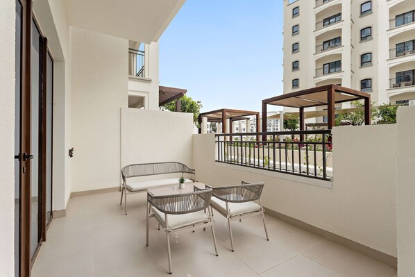 A balcony with a table and chairs, a view of a building, and a railing. - Silkhaus Vacation Homes Prime 2BR in Yas Golf Collection (Abu Dhabi)