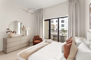 A hotel room with a bed, a dresser, a chair, a round table, and a balcony with a view of buildings. - Silkhaus Vacation Homes Prime 2BR in Yas Golf Collection (Abu Dhabi)