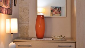 Et soveværelse med en seng, en sengetavlelampe, en kommode med skuffer, et spejl og en vase på kommoden.