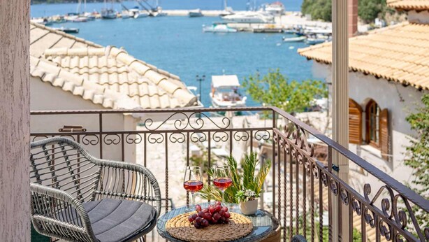 A balcony with wicker chairs, a small table with a glass of red wine, and a view of a marina with boats. - Esperides Estia - Sea View Syvota Stay w Balcony (Igoumenitsa)