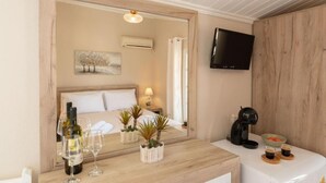 A hotel room with a bed, bedside table with wine glasses and a bottle, a coffee machine, a TV, and a painting on the wall. - Esperides Estia - Sea View Syvota Stay w Balcony (Igoumenitsa)
