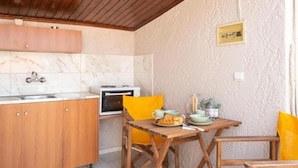 A kitchen with wooden cabinets, a marble backsplash, a microwave, and a dining table with chairs. - Esperides Estia - Sea View Syvota Stay w Balcony (Igoumenitsa)