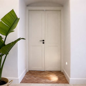 A white double door with a modern handle, a potted plant to the left, and a herringbone-patterned floor. - Thomais - Refined Living in the Heart of Mykonos (Mykonos)