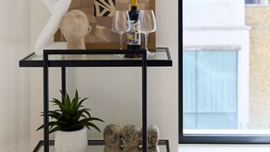 Uma sala de estar moderna com uma mesa de centro de vidro, um vaso de planta, uma escultura e uma obra de arte emoldurada.