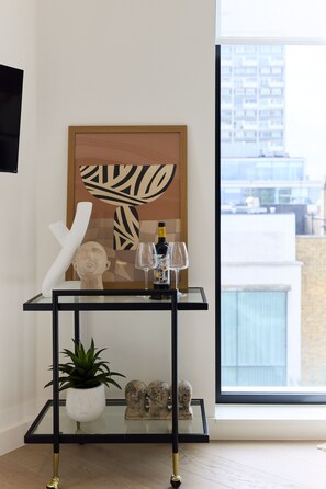 Een moderne woonkamer met een glazen salontafel, een potplant, een sculptuur en een ingelijste kunstwerk.