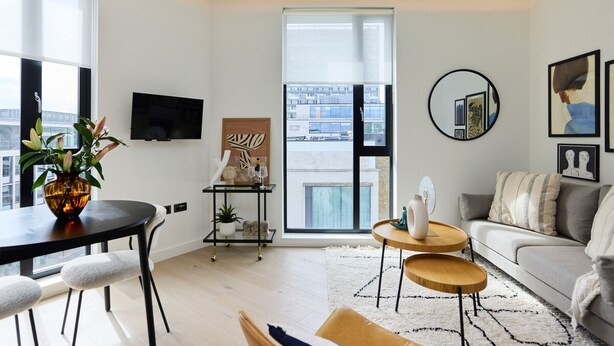 Uma sala de estar moderna com sofá, mesa de centro, televisão e uma janela grande com vista para prédios.