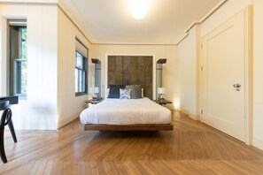 A bedroom with a large bed, wooden flooring, a window, a desk, and a door. - 10a OG Primrose Hill Townhouse-industrial Chic Design 10 (London)