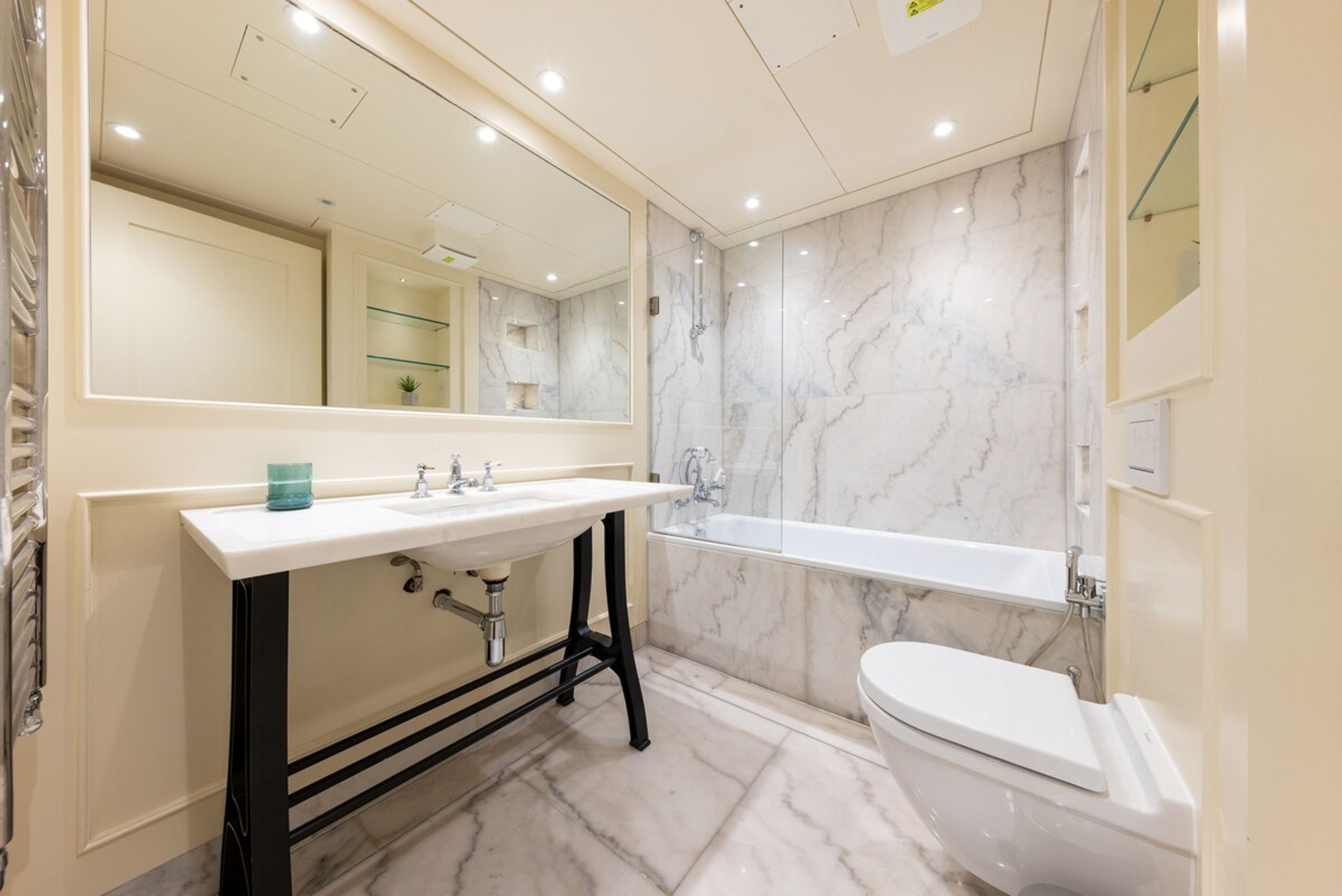 A modern bathroom with a marble sink, a large mirror, a bathtub, and a toilet.