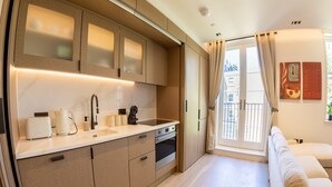 A modern kitchen with built-in appliances, a dining area with a sofa, and a view through a large window. - The Pembridge 11 (London)