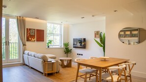 A modern living room with a sofa, dining table, chairs, a TV, and a large window. - The Pembridge 11 (London)