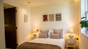 Ein Schlafzimmer mit einem Bett, Nachttischlampen, einem Beistelltisch, einer Tür und Wandbildern.