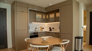A modern kitchen with wooden cabinets, a round dining table with chairs, and a stainless steel trash bin. - Pembridge Residences - Flat 3 (London)