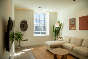 A living room with a sofa, a coffee table, a potted plant, a TV, and a window. - Pembridge Residences - Flat 3 (London)