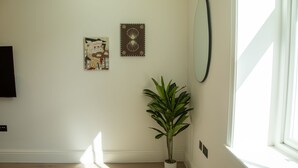 A room with a potted plant, a wall-mounted mirror, and two framed artworks. - Pembridge Residences - Flat 3 (London)