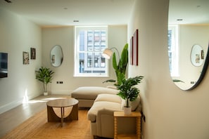 A modern living room with a sofa, coffee table, potted plants, and a large window. - Pembridge Residences - Flat 3 (London)