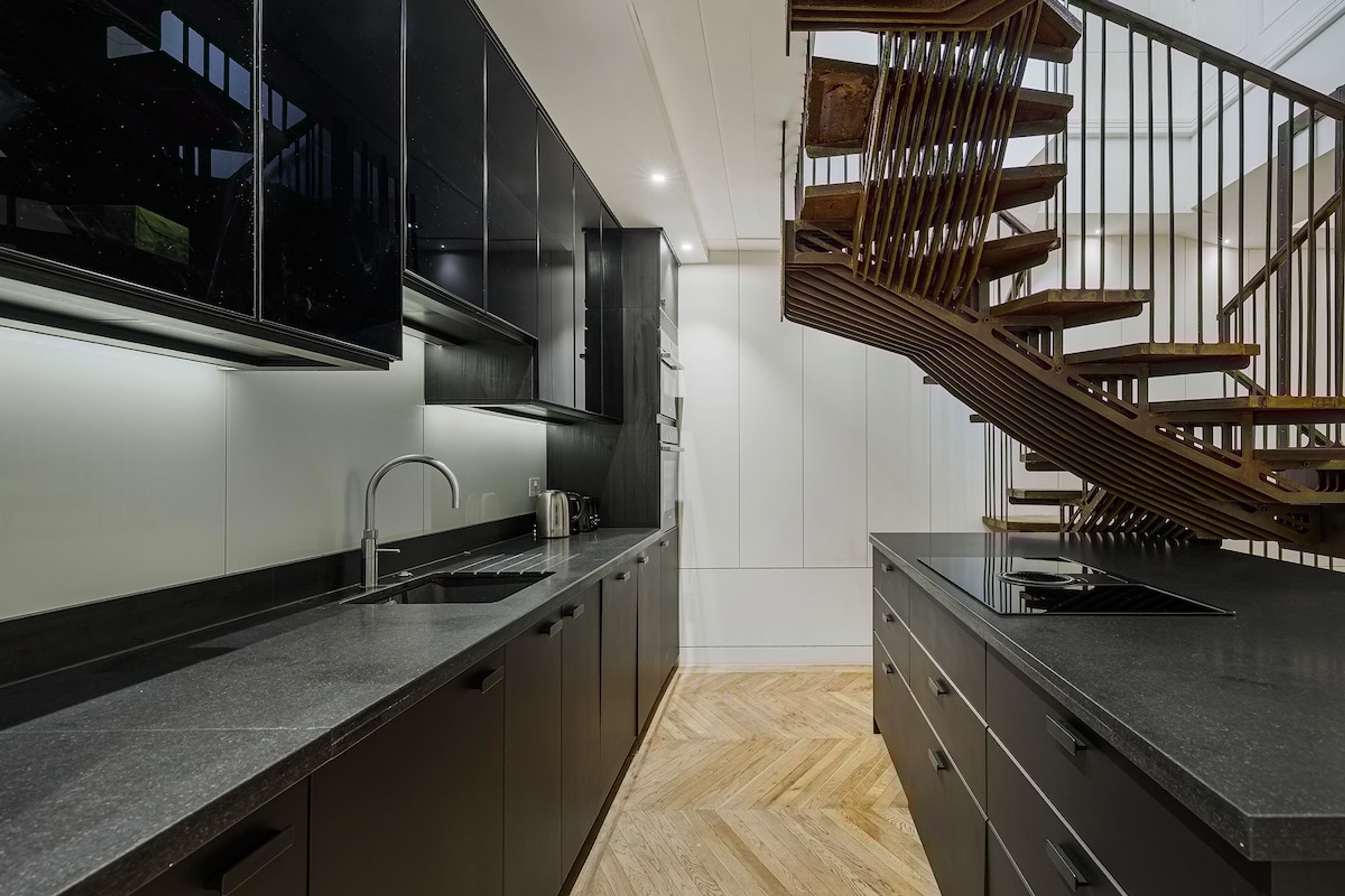 Una cocina moderna con armarios oscuros, una escalera de madera y un ventanal grande.