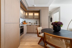 A modern kitchen with wooden cabinets, a dining table with chairs, and a potted plant. - The Pembridge Residences Modern Notting Hill 9b (London)