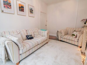 A living room with two striped sofas, a teal throw pillow, and a 'LOVE' pillow. There are framed pictures on the wall and a door in the background. - 50 Gladstone Avenue (Chester)