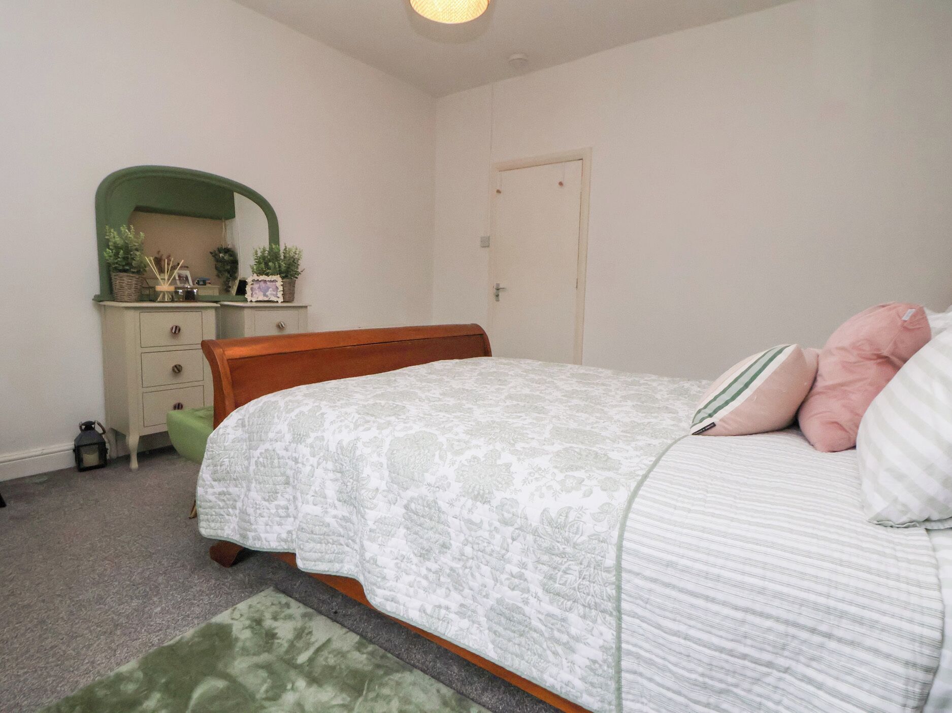 A bedroom with a bed, a dresser, a mirror, and a door.