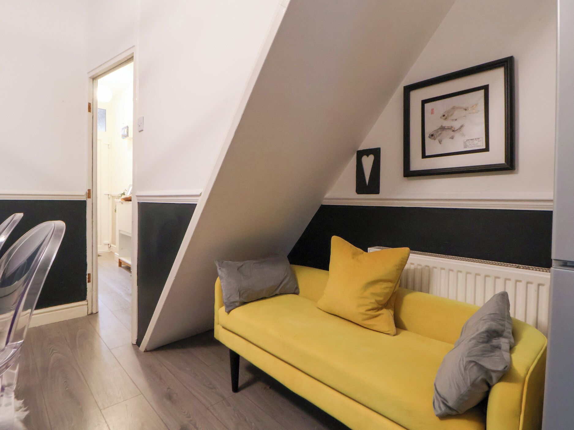 A room with a yellow sofa, a white radiator, and a framed picture on the wall.