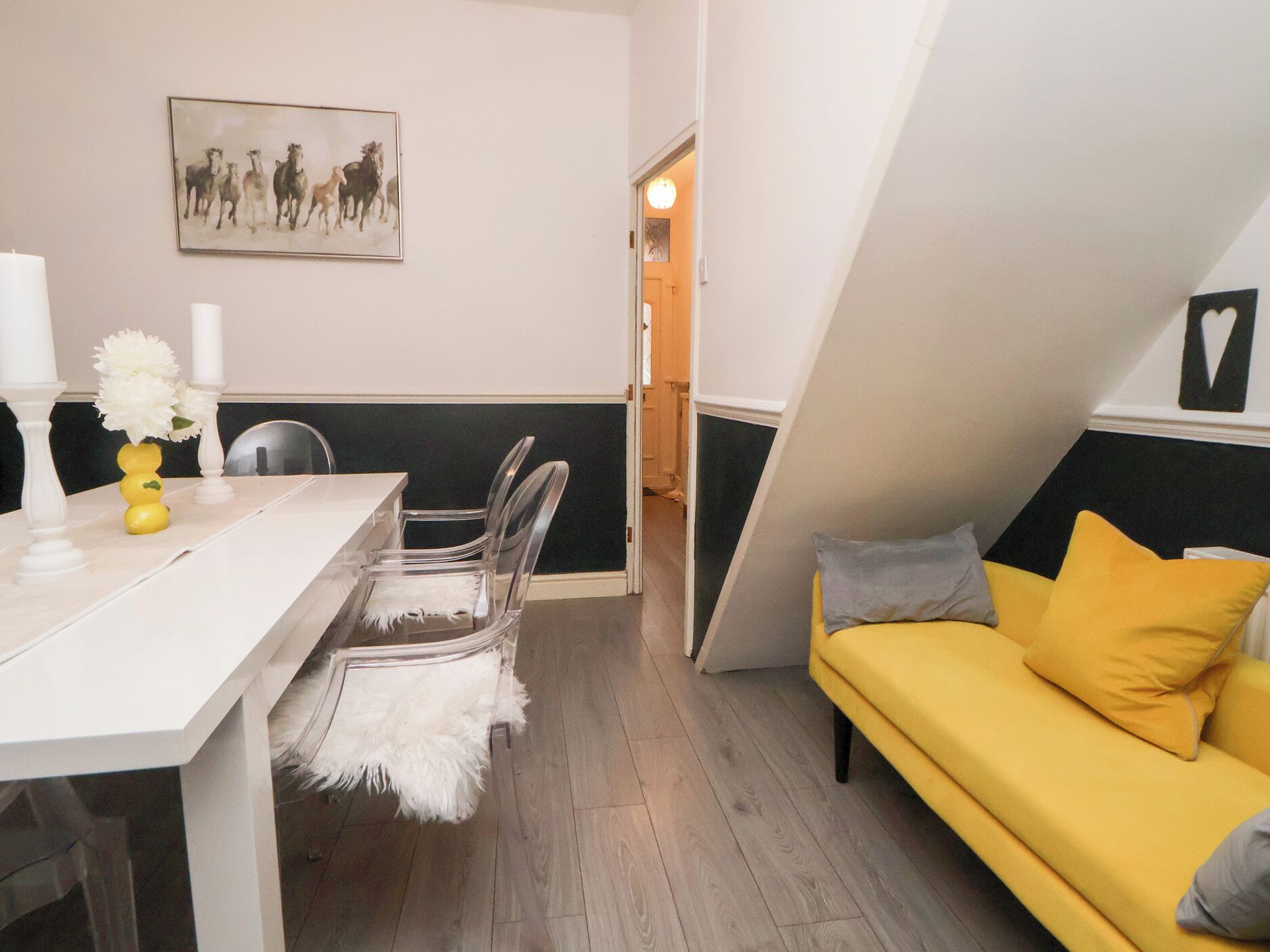 A room with a dining table, chairs, a yellow sofa, and a painting on the wall.