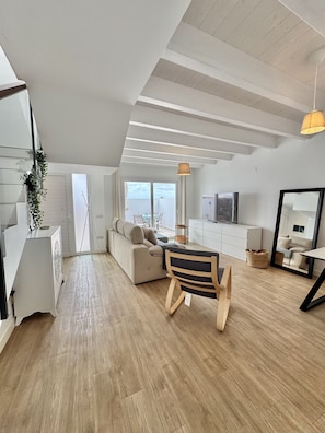 A modern living room with a sofa, a dining table with chairs, a TV, and a large window. - Casahost Dolce Vita Villa Eira (Costa Teguise)