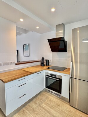 Eine moderne Küche mit weißen Schränken, einem Edelstahl-Kühlschrank, einem eingebauten Backofen und einer Holzausziehtafel.