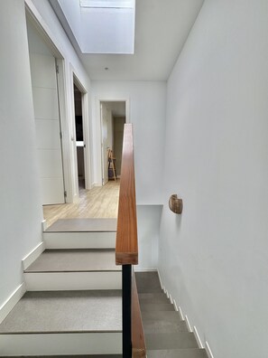 Eine Treppe mit hölzernem Geländer führt zu einer Empore, mit weißen Wänden und einem Oberlicht darüber.