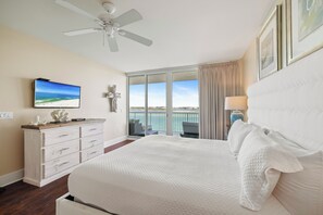 Ein Hotelzimmer mit einem großen Bett, einem Deckenventilator, einem an der Wand befestigten Fernseher, einem Schminktisch und einem Balkon mit Meerblick.