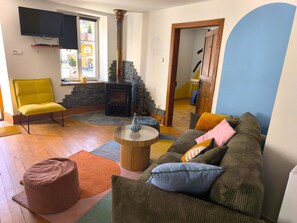 Ein Wohnzimmer mit einer Couch, einem Sessel, einem kleinen Tisch, einem Kamin aus Stein und einem an der Wand befestigten Fernseher.