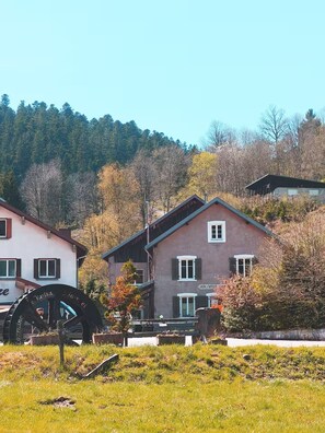 Un bâtiment doté d’une grande roue à eau, entouré de verdure et d’arbres.