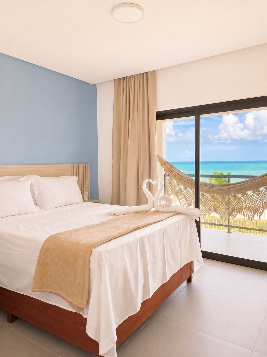 A hotel room with a bed, a view of the ocean, and a hammock.