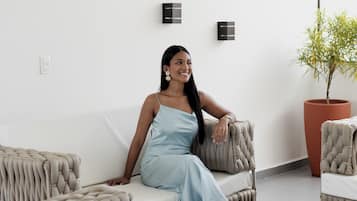 Una persona sentada en un sofá en una habitación con una planta en maceta y una lámpara fijada a la pared.