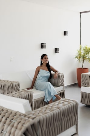 A person seated on a sofa in a room with a potted plant and a wall-mounted light fixture.