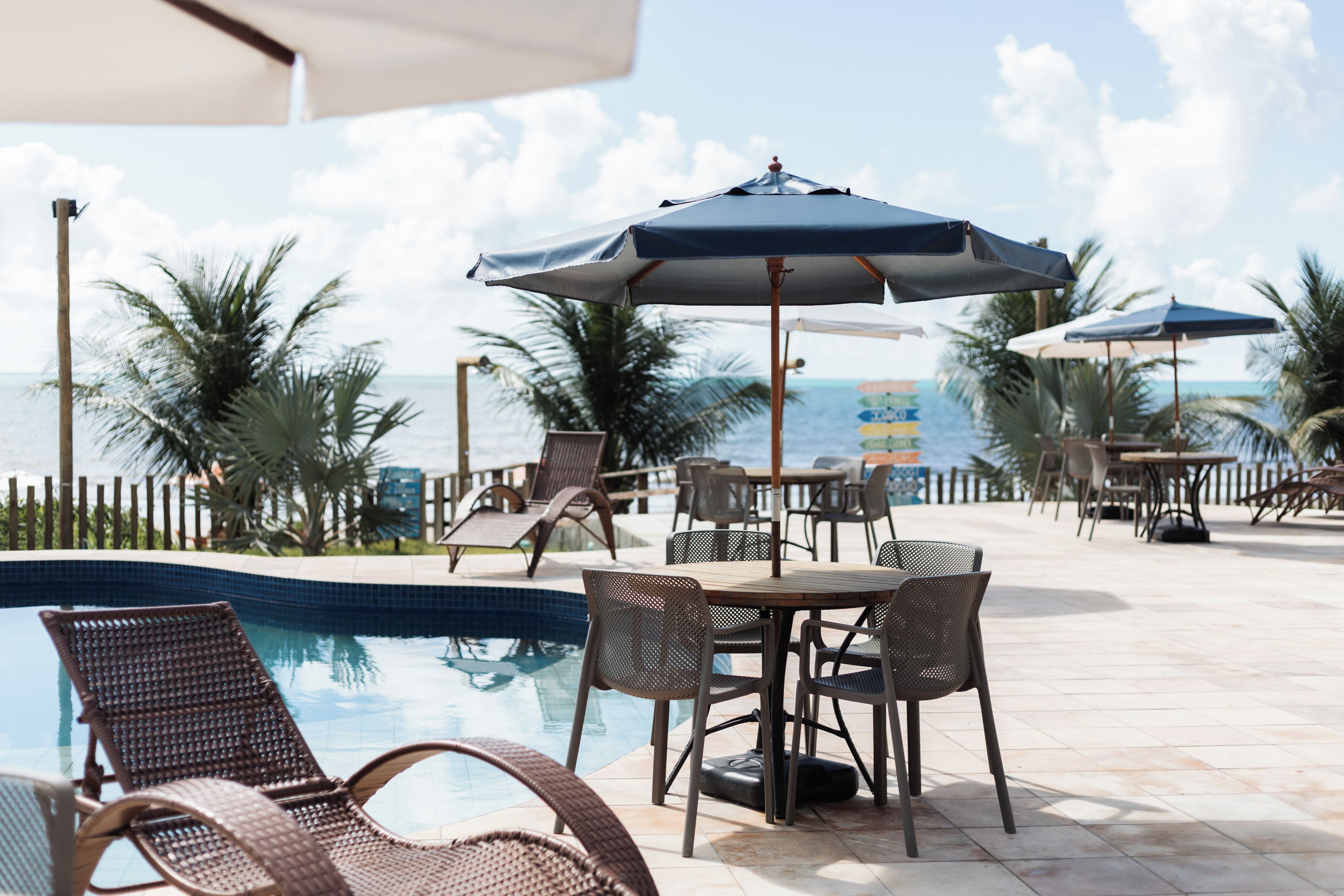 A poolside area with lounge chairs and umbrellas, overlooking a clear view of the ocean.