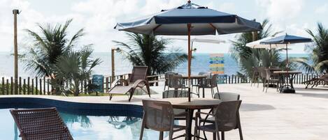 A poolside area with lounge chairs and umbrellas, overlooking a clear view of the ocean.
