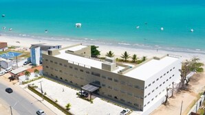 Um hotel de vários andares com telhado plano, área de estacionamento e vista para a praia e oceano.
