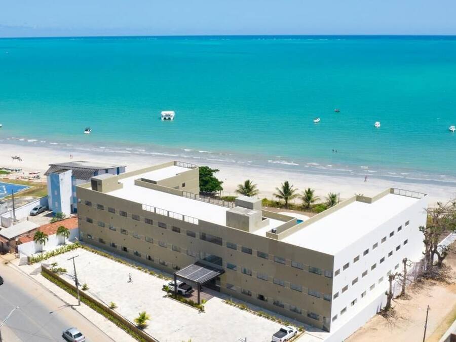 Un hotel de diversos pisos amb un terrat pla, una zona d'aparcament i vistes a la platja i l'oceà.