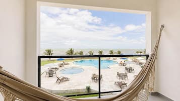 A hammock in a room with a view of a pool and beach.