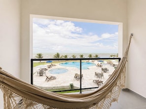 A hammock in a room with a view of a pool and beach.