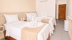 Habitación de hotel con una cama grande, dos camas más pequeñas, un cabecero de madera, una pared blanca, una puerta de madera y un equipo de aire acondicionado blanco.