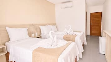 Habitación de hotel con una cama grande, dos camas más pequeñas, un cabecero de madera, una pared blanca, una puerta de madera y un equipo de aire acondicionado blanco.