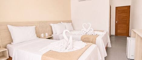 Habitación de hotel con una cama grande, dos camas más pequeñas, un cabecero de madera, una pared blanca, una puerta de madera y un equipo de aire acondicionado blanco.