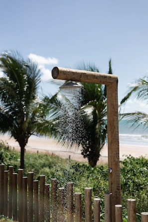 A wooden structure with a water spout, surrounded by greenery and palm trees, overlooking a beach.
