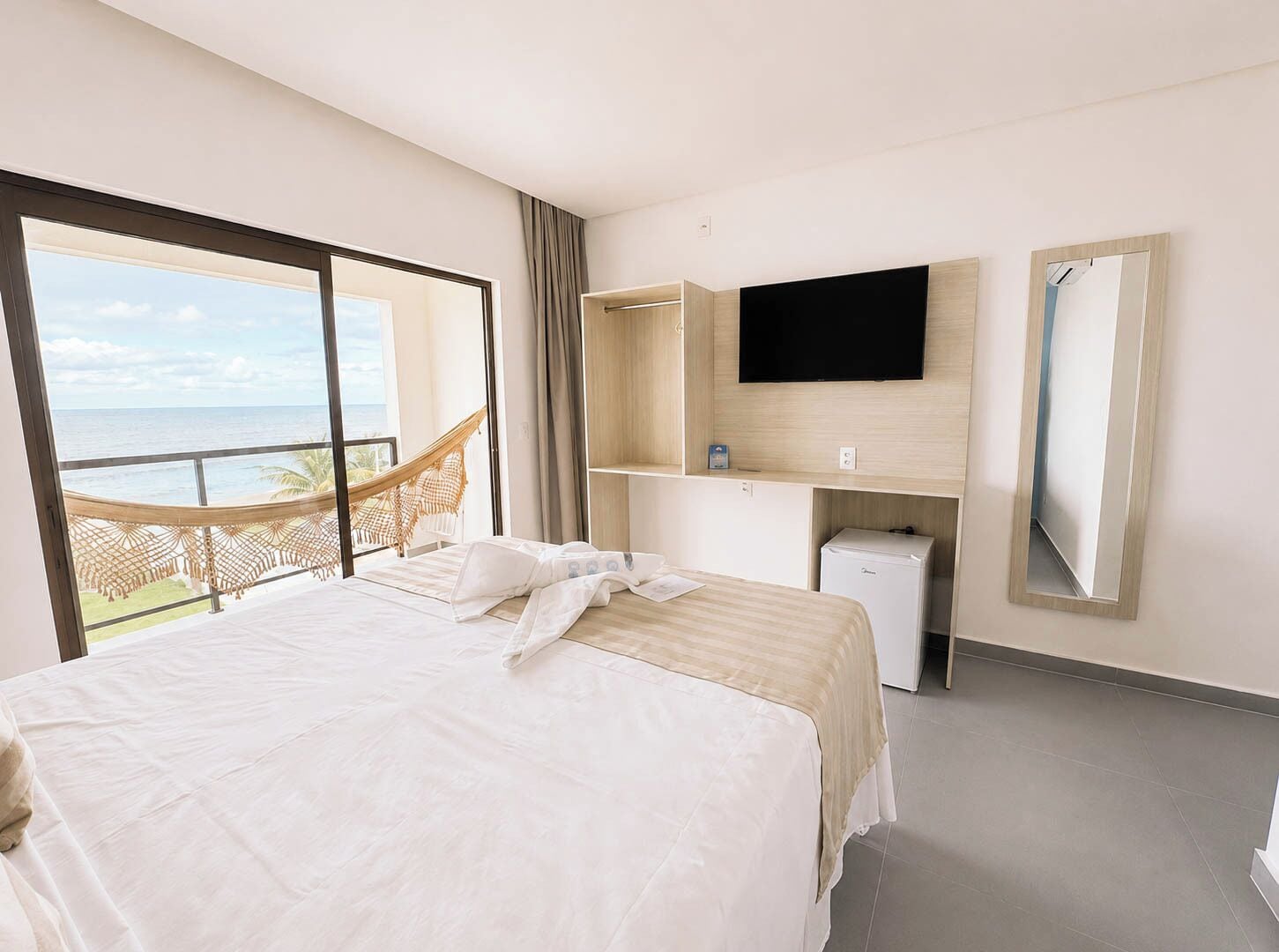 Quarto de hotel com cama, televisão, minibar e vista para o oceano.