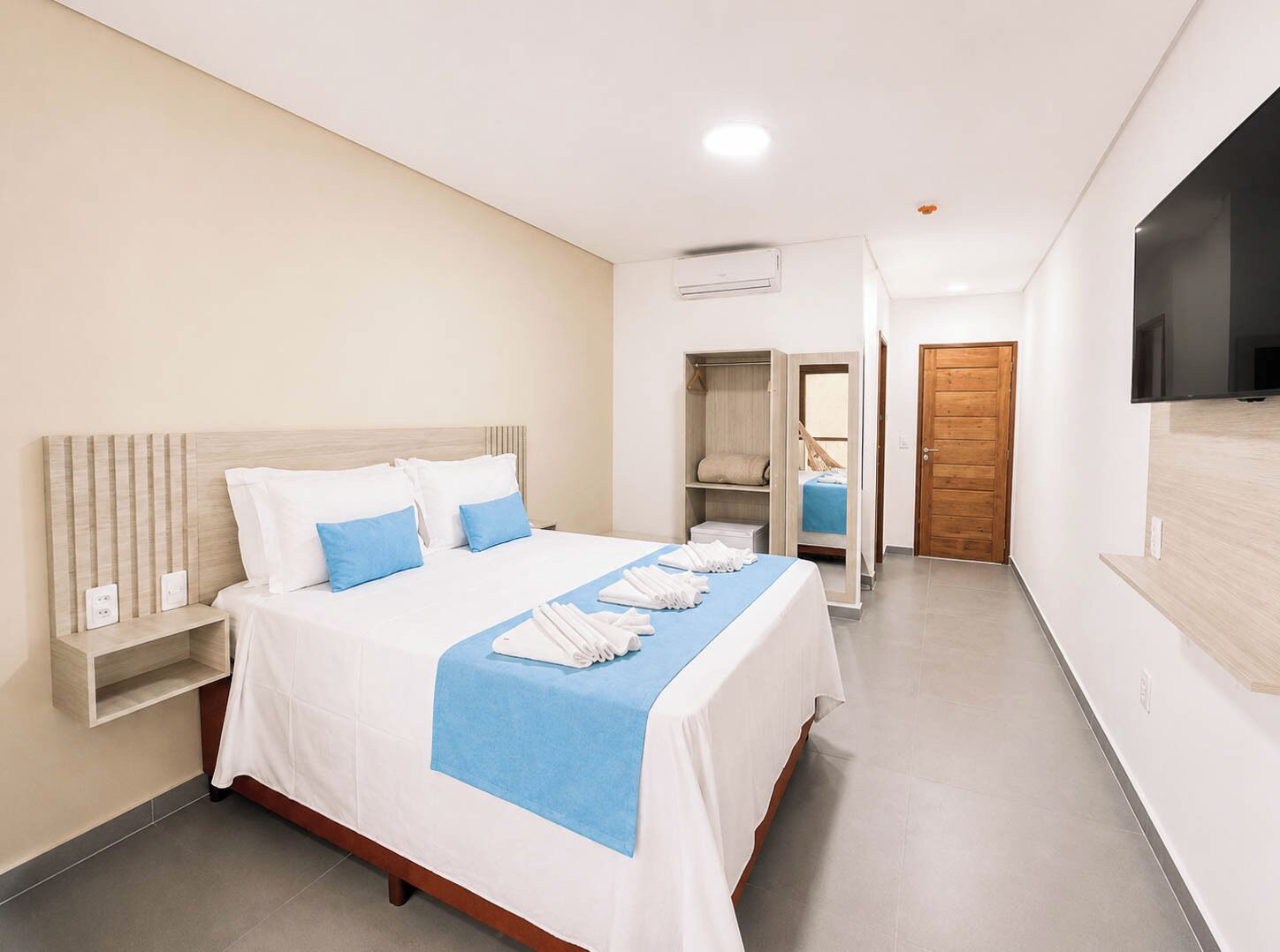 Una habitación de hotel con cama, armario, televisor y puerta.