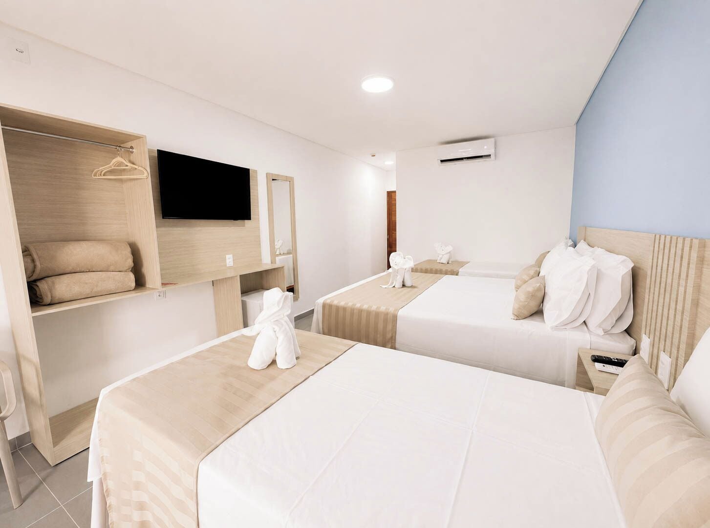 Habitación de hotel con dos camas, televisor, armario y espejo.